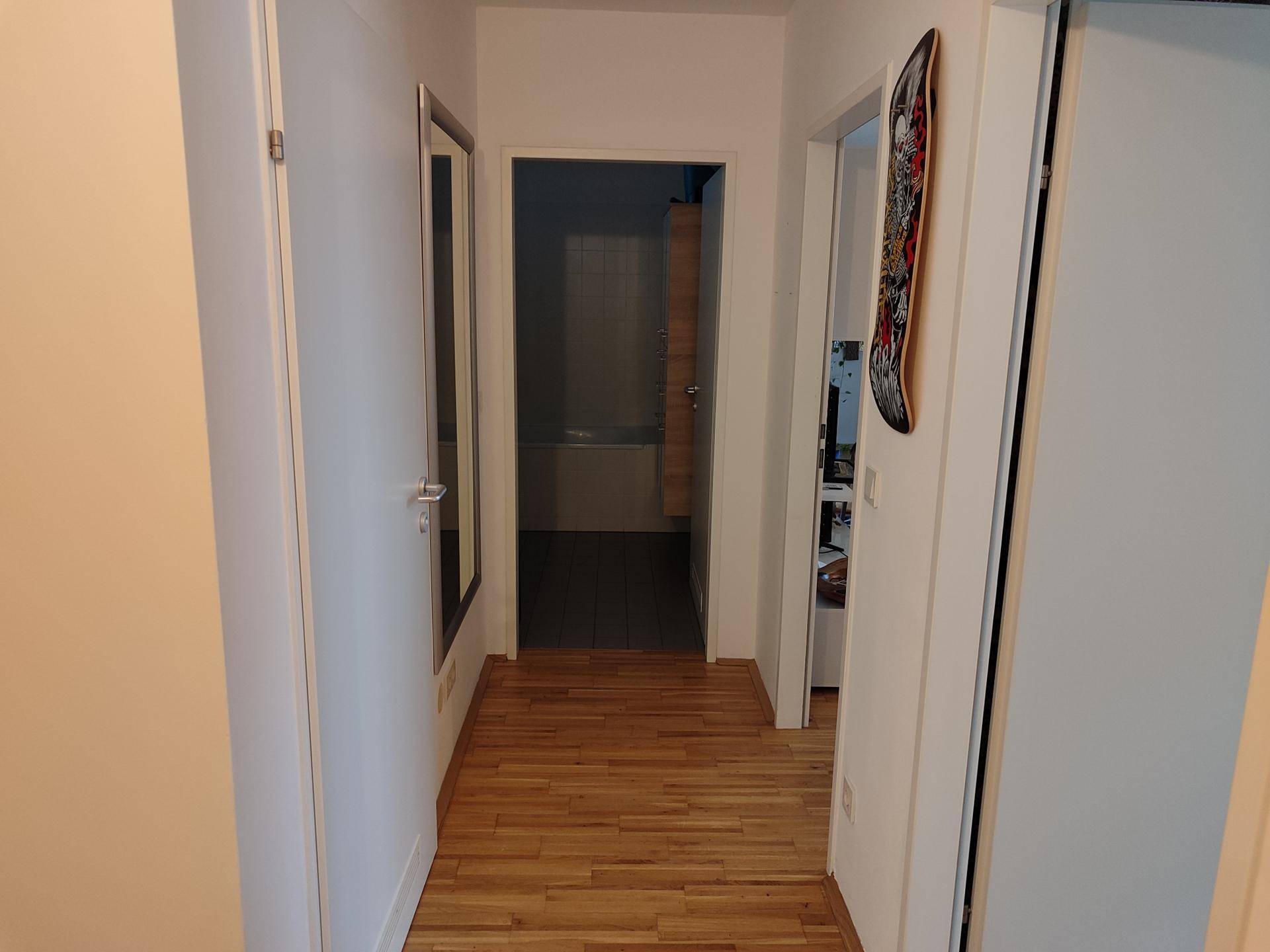 Langer Flur mit hellem Parkettboden und einem großen Wandspiegel.