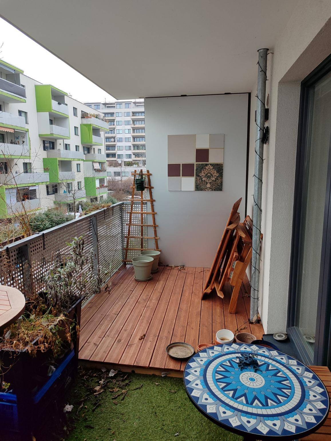 Balkon mit Holzbelag, Sitzgelegenheiten und Blick auf die umliegenden Gebäude.