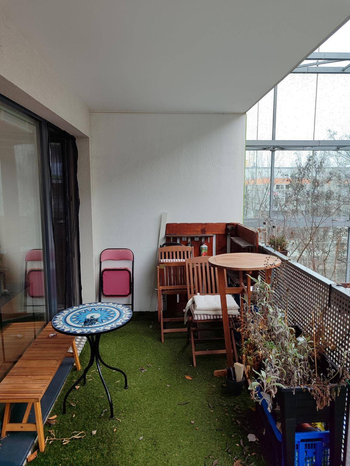 Balkon mit Kunstrasen, gemütlichen Gartenmöbeln und Blick auf die Umgebung.