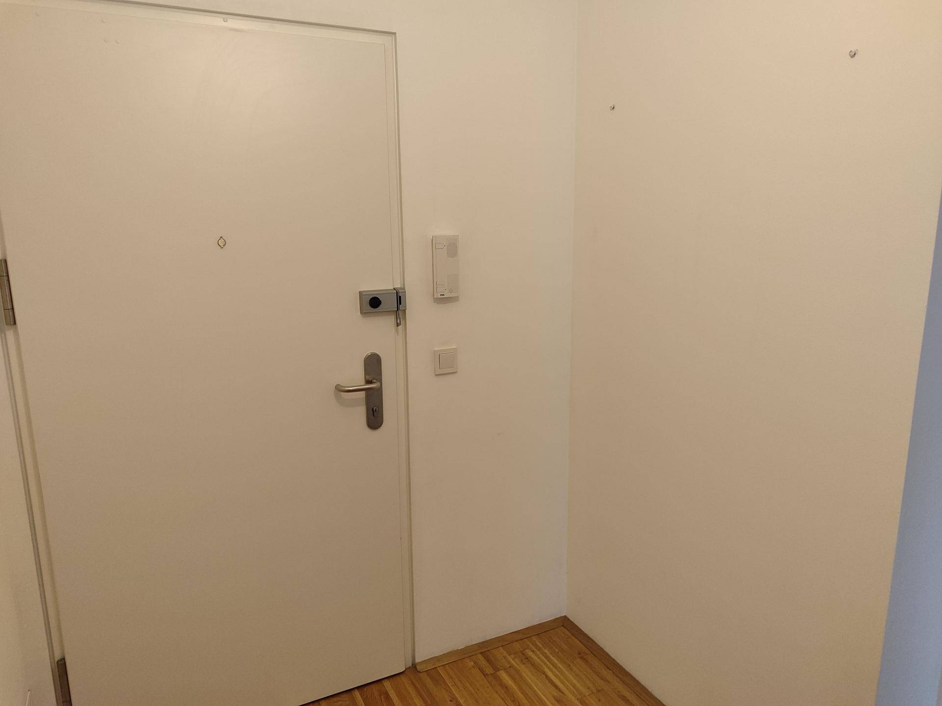 Helle Eingangstür mit Gegensprechanlage in einem schlichten Flur.