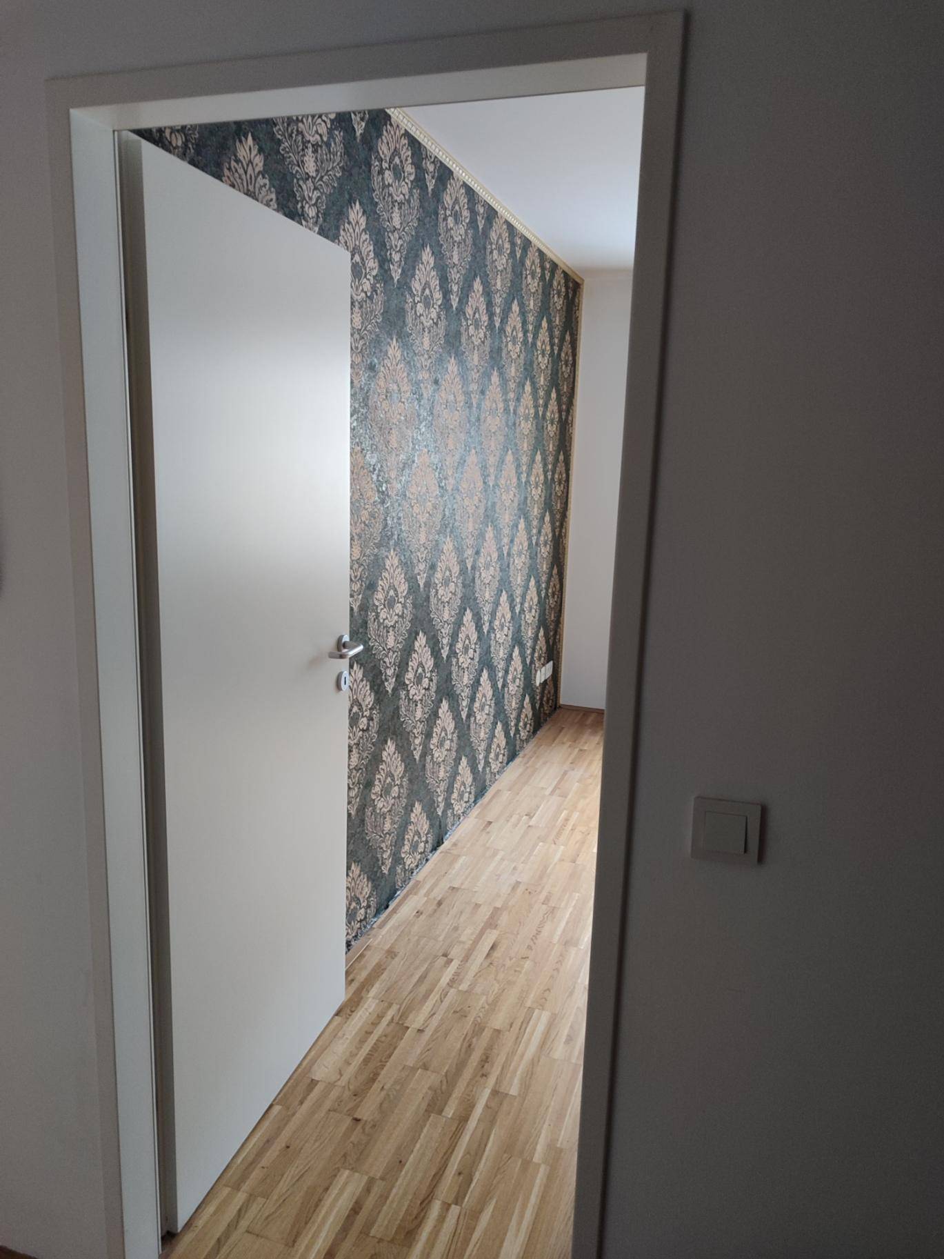 Eingang zu einem Schlafzimmer mit auffälliger Mustertapete und Parkettboden.