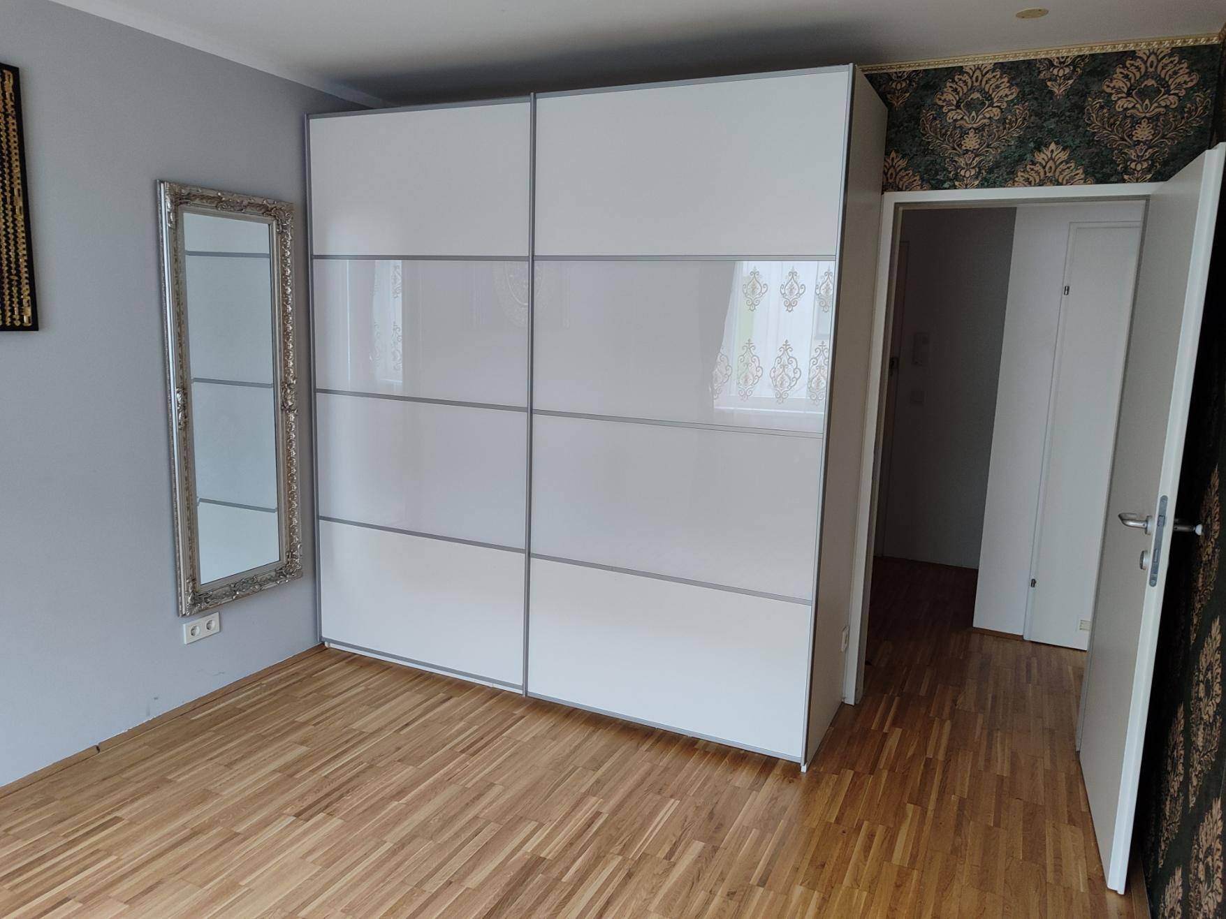 Schlafzimmer mit großem weißen Schiebetürenschrank und Parkettboden.