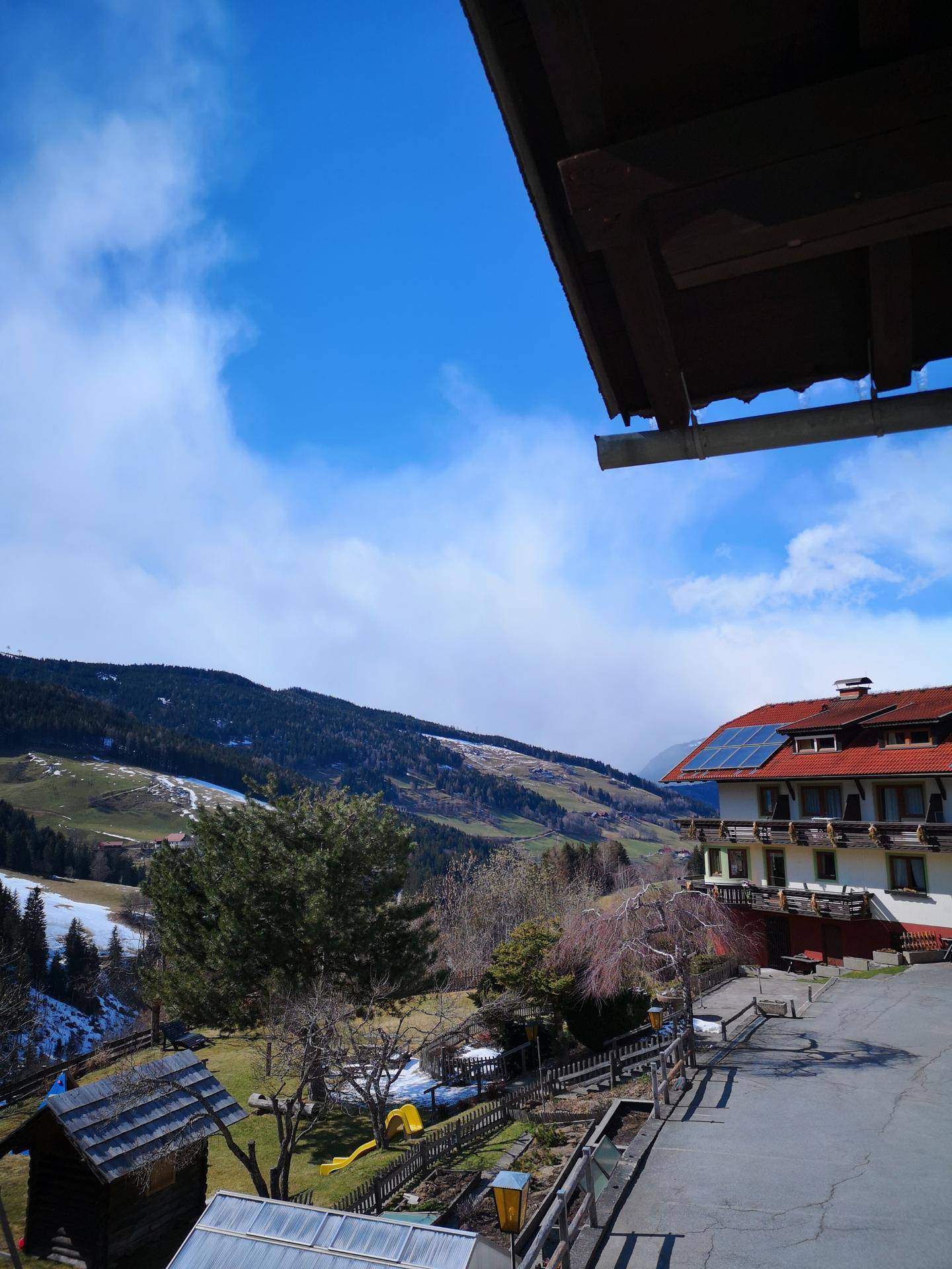 Blick von einem Garten auf eine weite Berglandschaft mit weiteren Gebäuden.