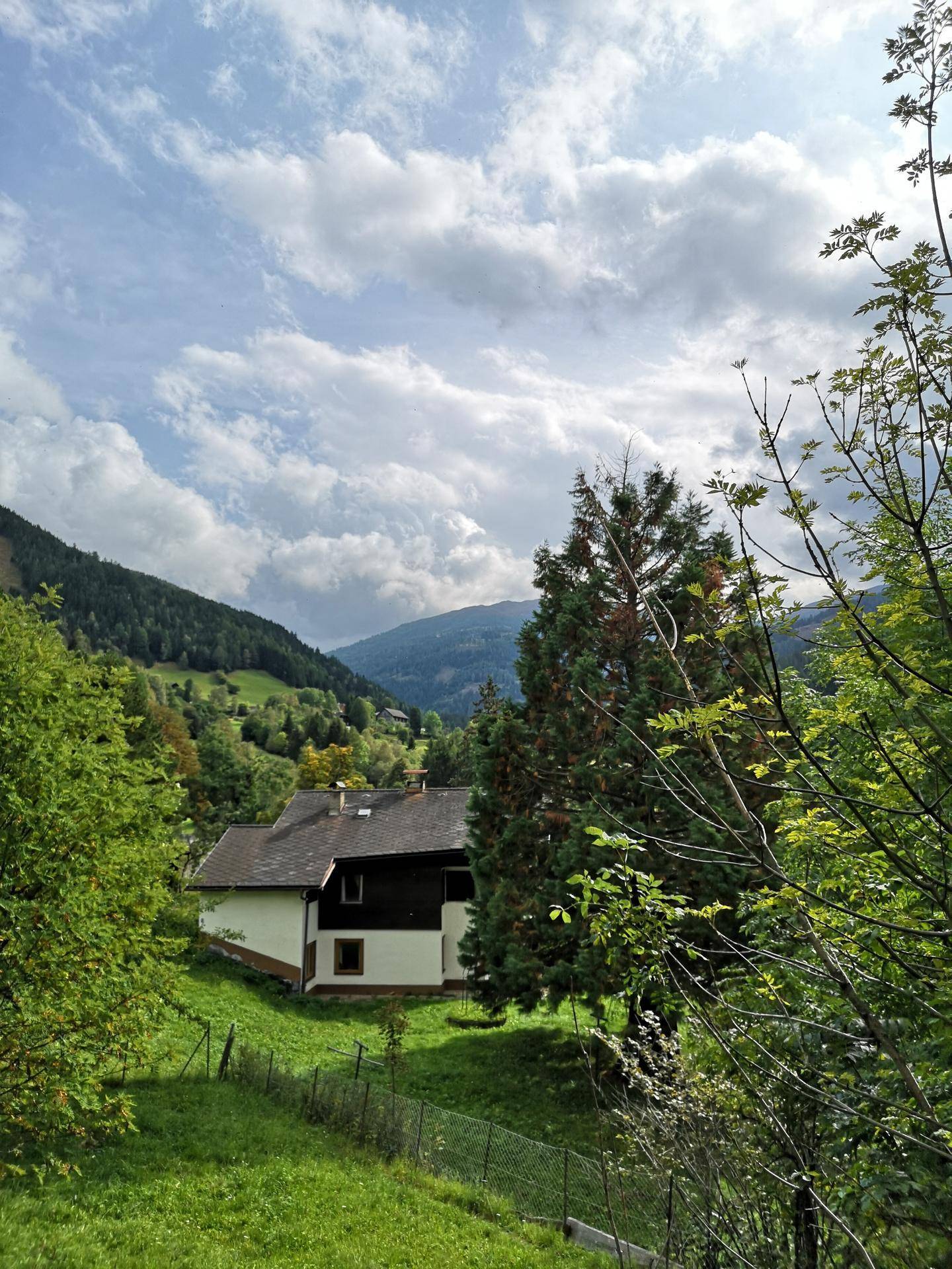Einfamilienhaus eingebettet in eine idyllische, grüne Berglandschaft unter bewölktem Himmel.