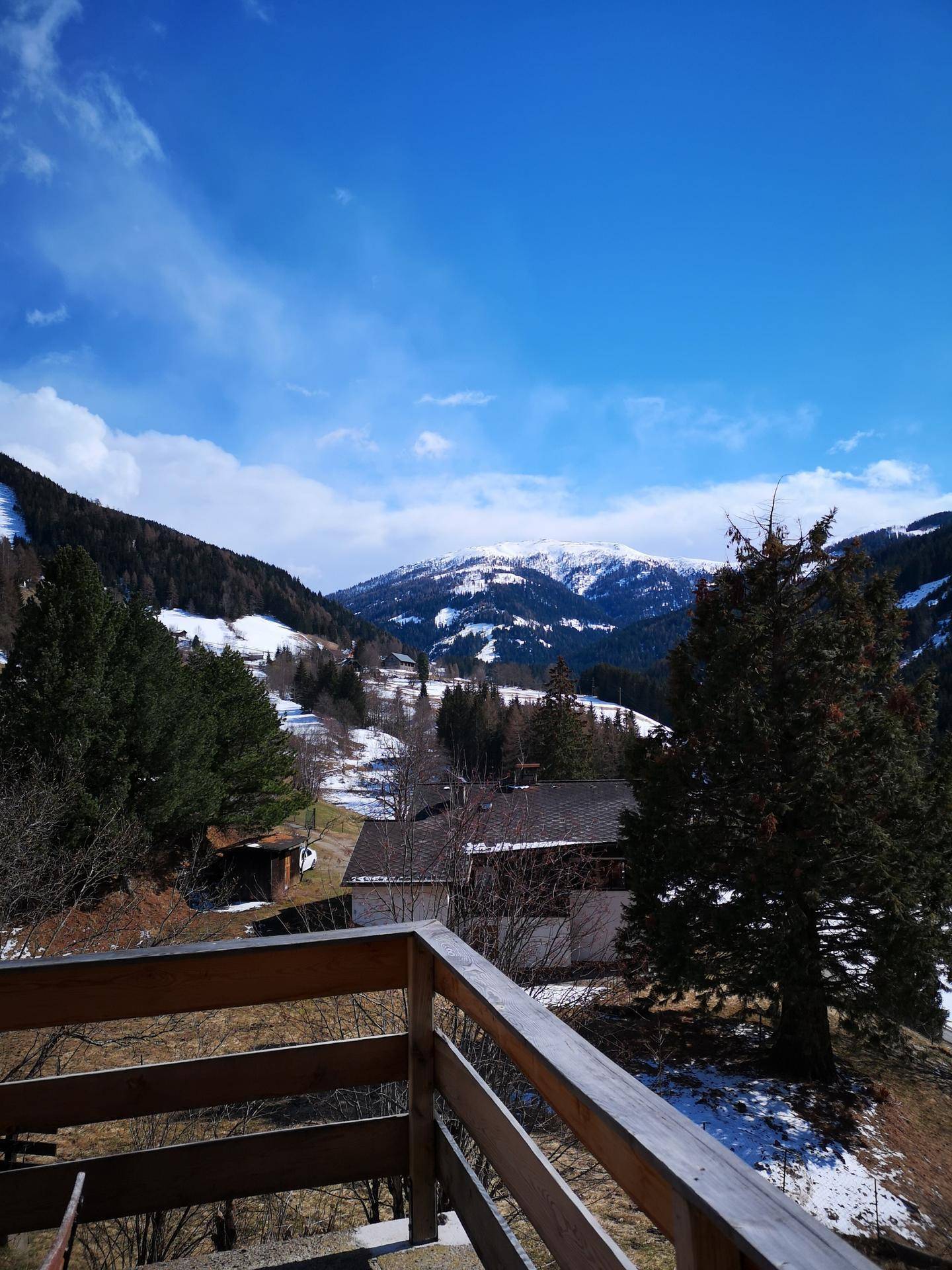 Panoramablick von einem Balkon auf schneebedeckte Berge und bewaldete Täler.