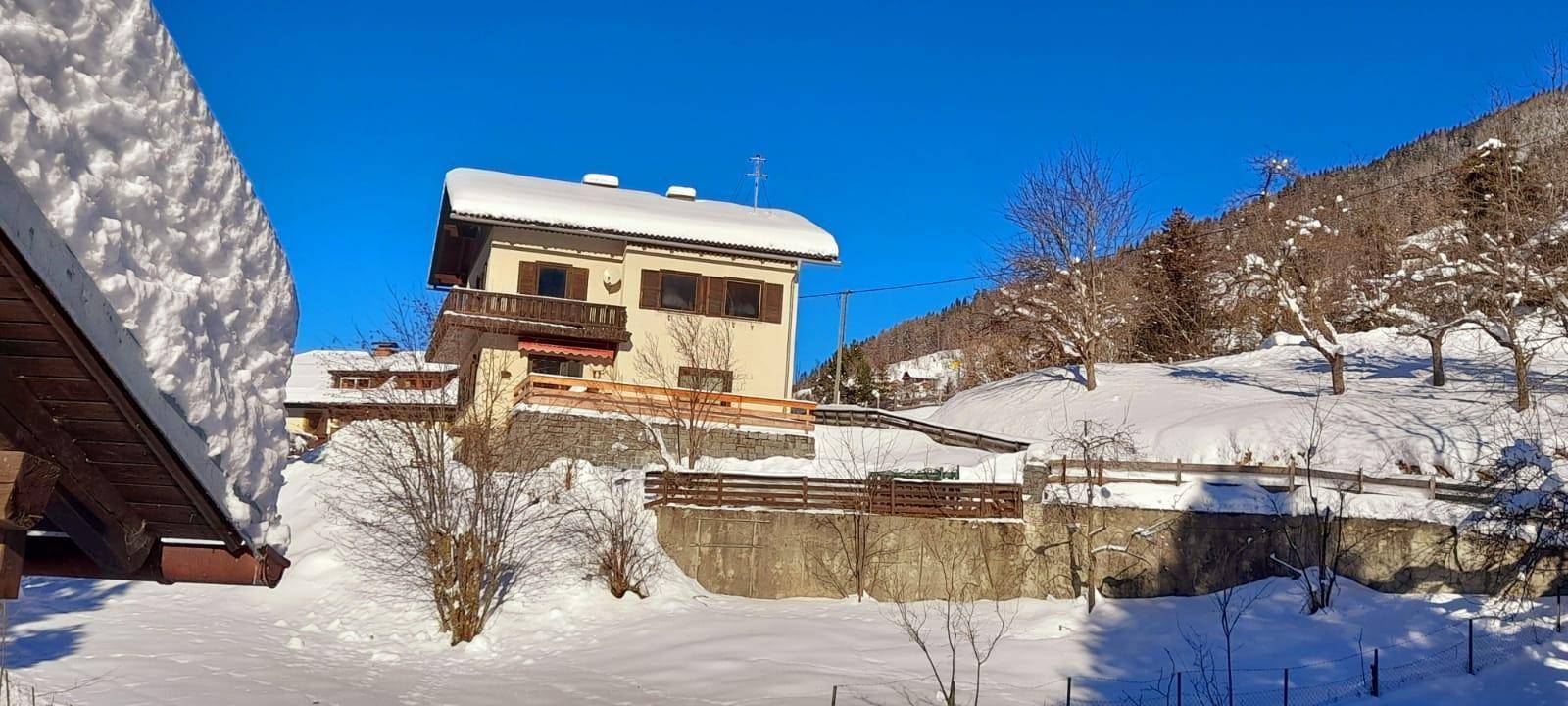 Haus in verschneiter Berglandschaft mit klarem blauem Himmel und sonniger Atmosphäre.