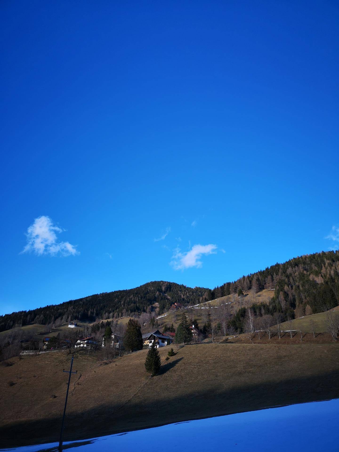 Weite Berglandschaft mit bewaldeten Hängen und schneebedeckten Flächen unter blauem Himmel.