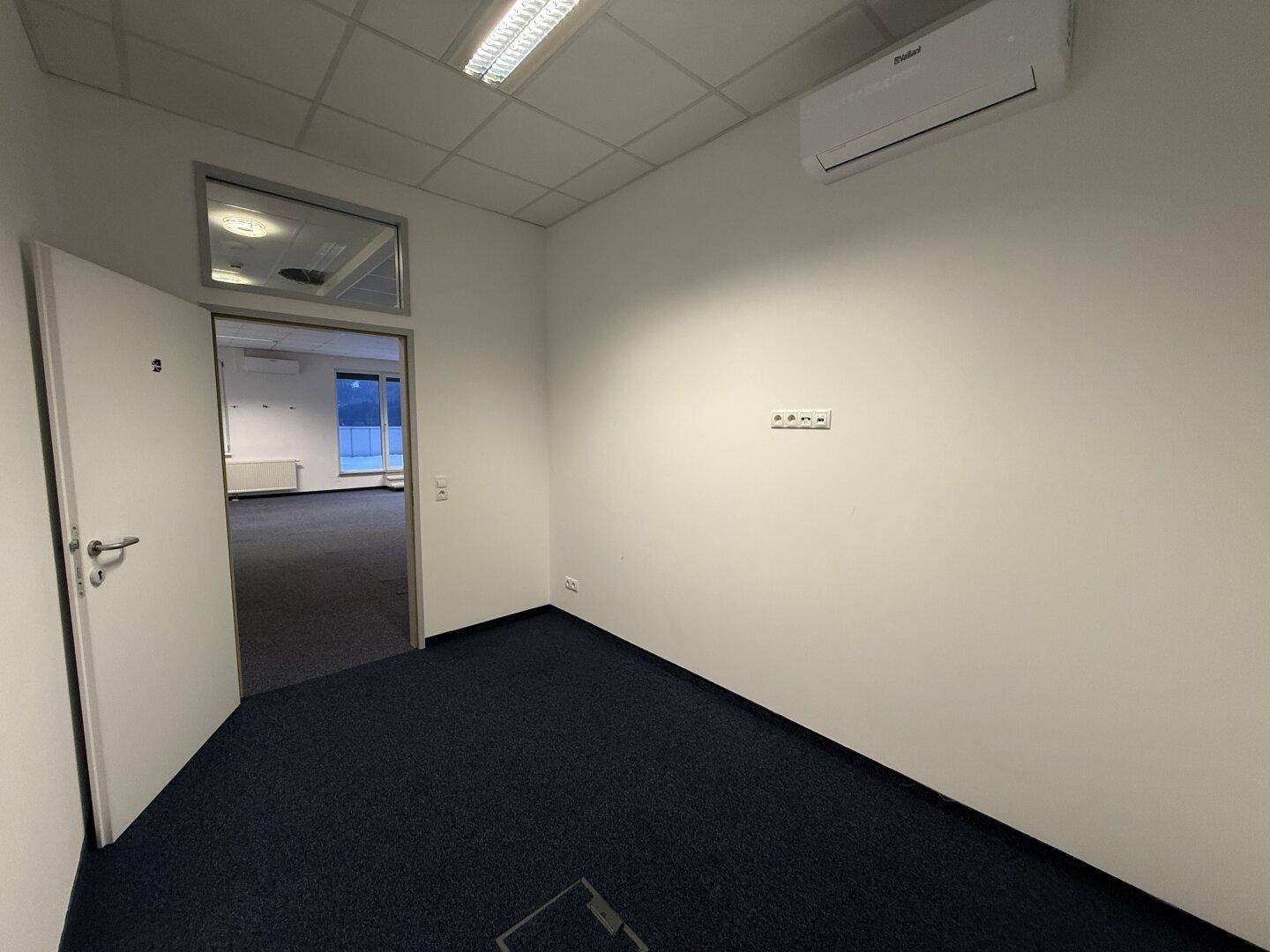 Büro mit Teppichboden und Klimaanlage, Blick durch die offene Tür in den Hauptbürobereich.
