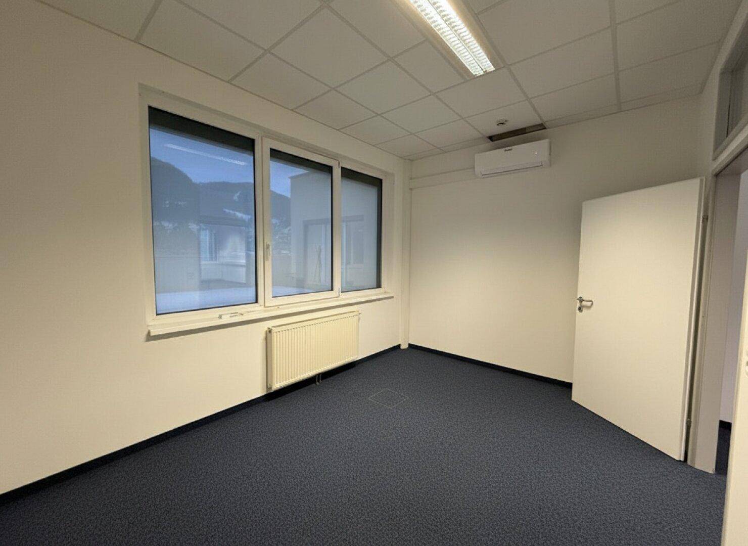 Kleineres Büro mit Teppichboden, Fenster und Klimaanlage, bereit zur individuellen Gestaltung.