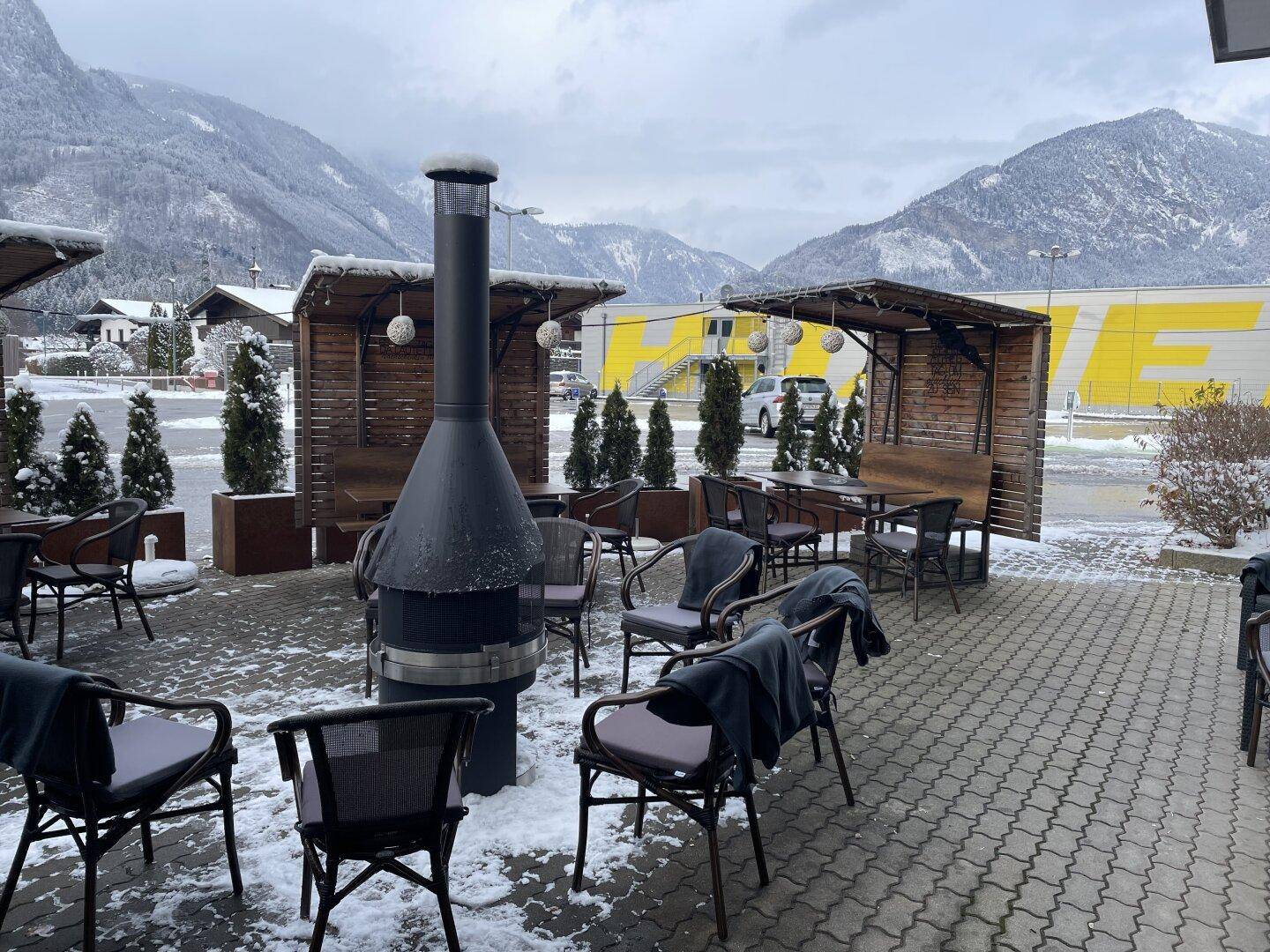 Gemütliche Außenterrasse mit Sitzgelegenheiten, Feuerstelle und Bergblick, bedeckt mit leichtem Schnee.