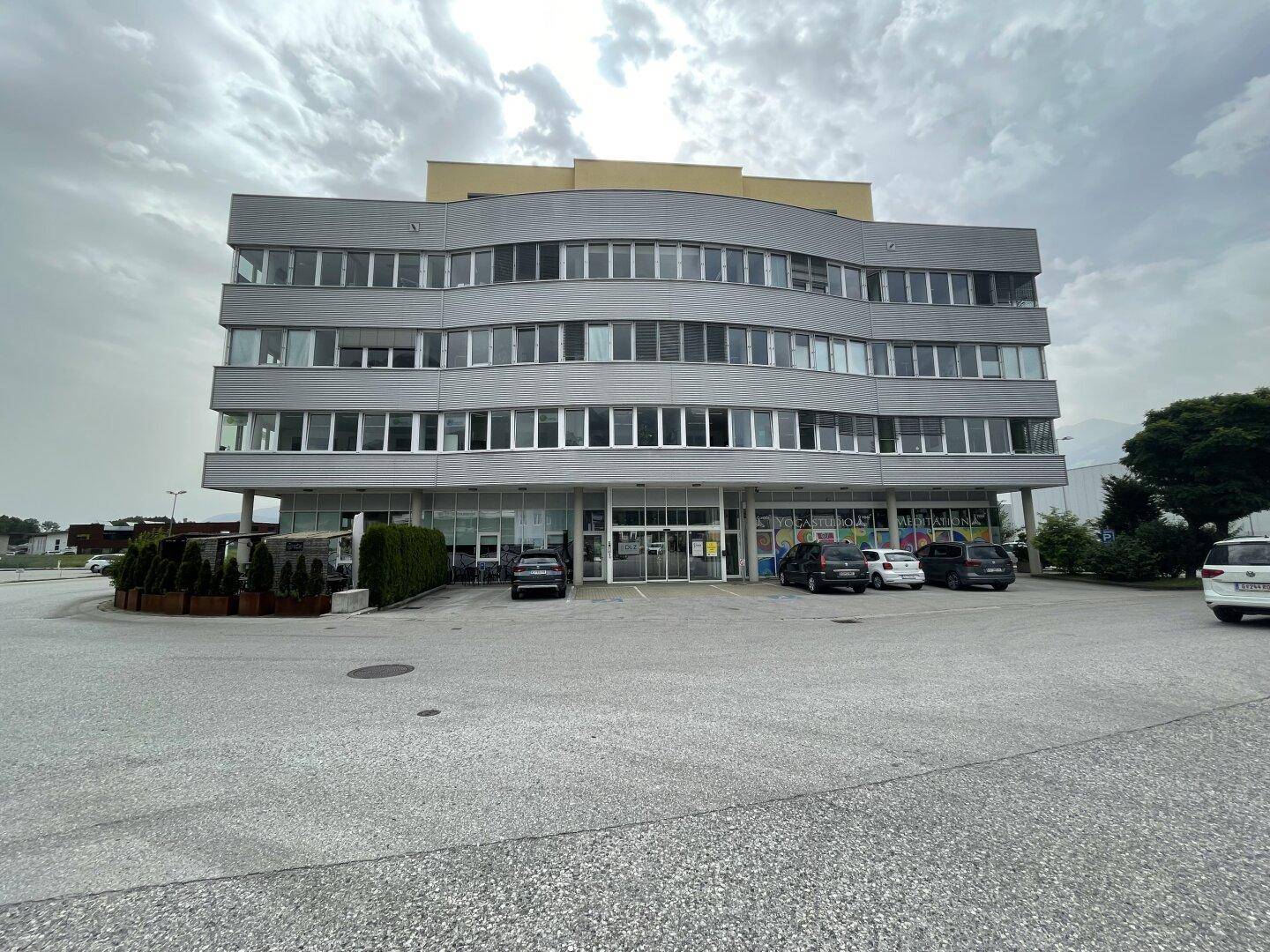 Modernes Geschäftsgebäude mit geschwungener Fassade, vielen Fenstern und Parkplätzen davor.