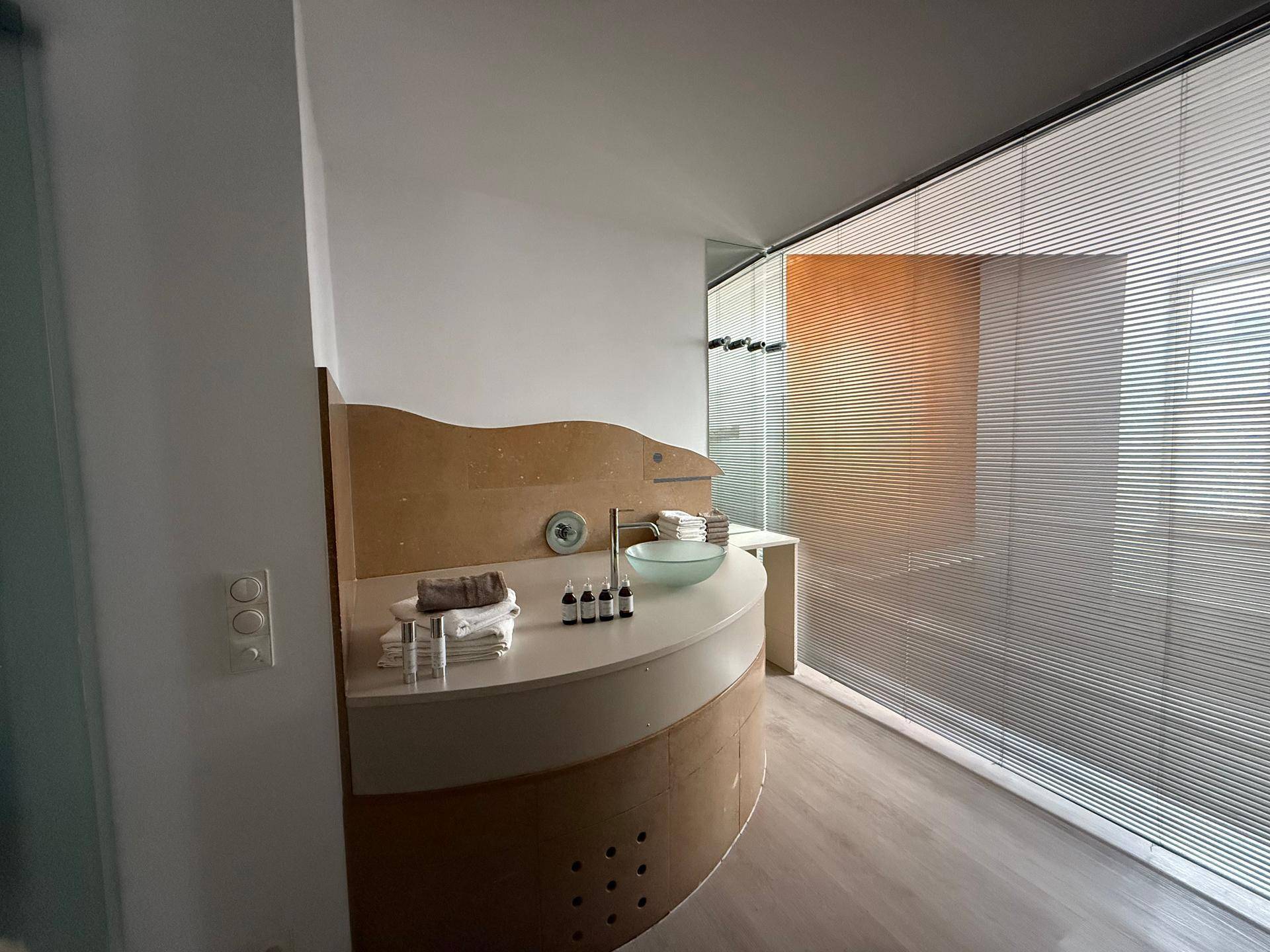 Modernes Badezimmer mit einem einzigartigen Waschbecken, Holzverkleidung und einem großen Fenster mit Jalousien.