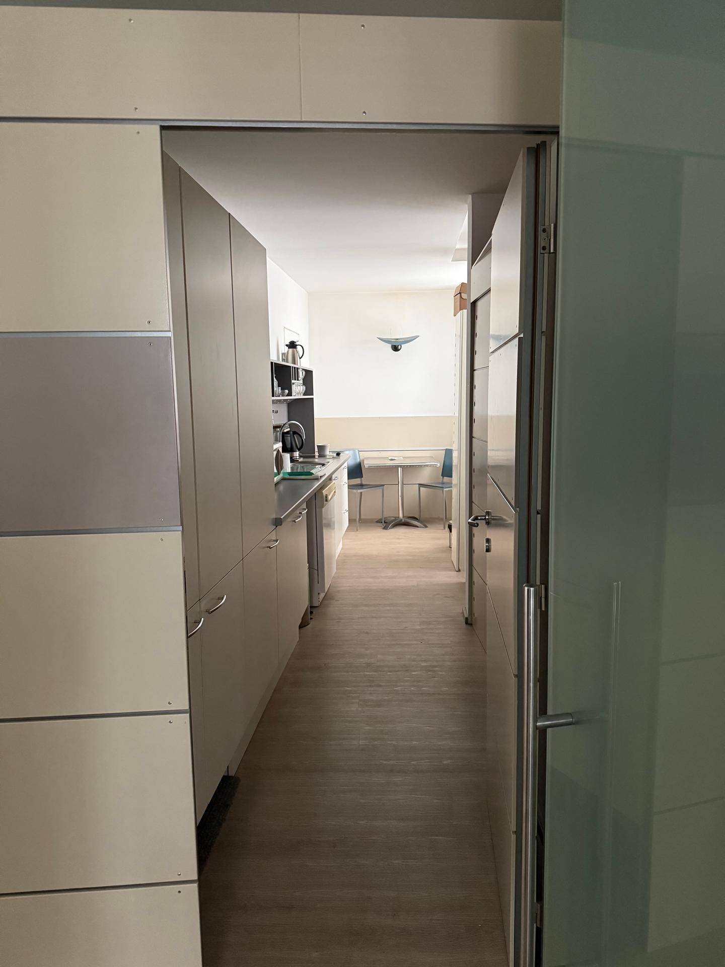 Schmaler Flur führt zu einer kleinen Küchenzeile mit Schränken und einem Tisch im Hintergrund.