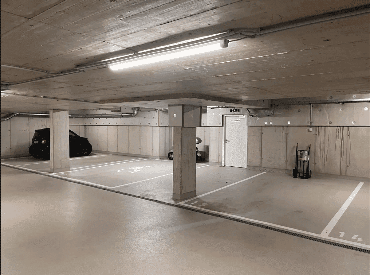 Tiefgarage mit Betonpfeilern, markierten Stellplätzen, darunter ein Behindertenparkplatz, und einem schwarzen Auto.
