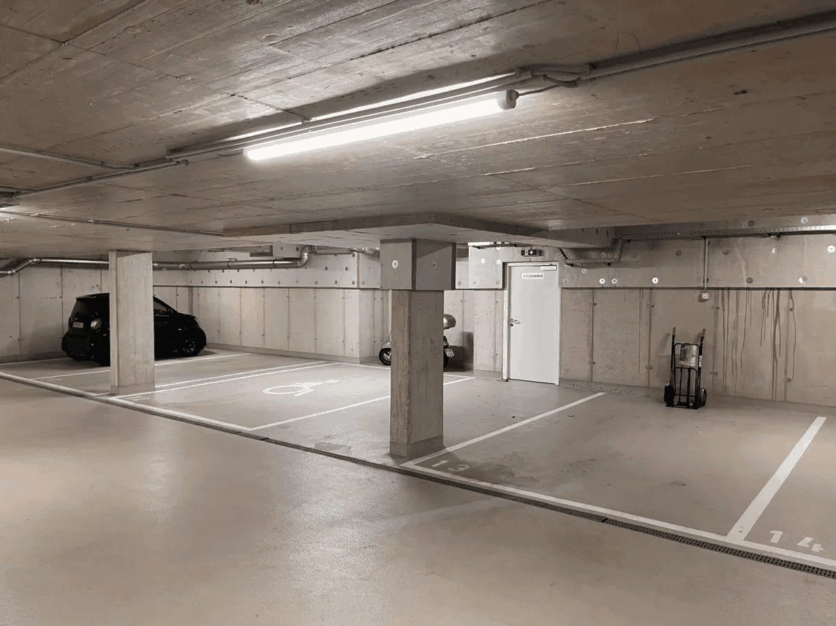 Tiefgarage mit Betonpfeilern, markierten Stellplätzen, darunter ein Behindertenparkplatz, und einem schwarzen Auto.