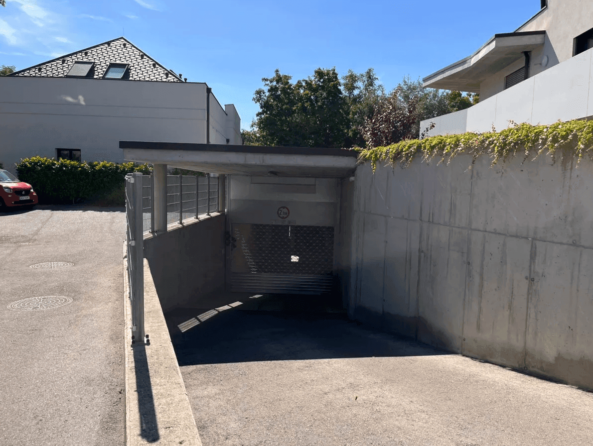 Außenansicht der Tiefgarageneinfahrt mit Betonwänden und begrüntem Dachbereich unter blauem Himmel.