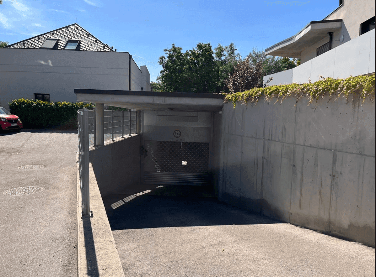 Außenansicht der Tiefgarageneinfahrt mit Betonwänden und begrüntem Dachbereich unter blauem Himmel.
