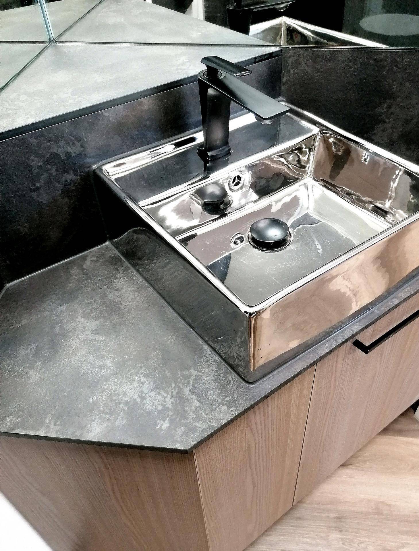 Modernes Waschbecken mit schwarzem Wasserhahn und dunkler Arbeitsplatte in einem Badezimmer.