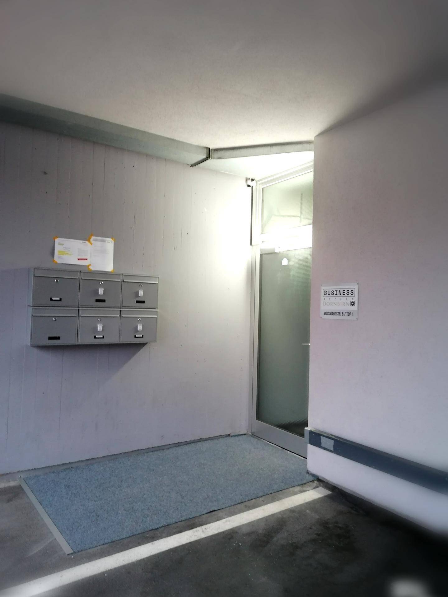 Eingangsbereich eines Geschäftsgebäudes mit Briefkästen und Glastür.