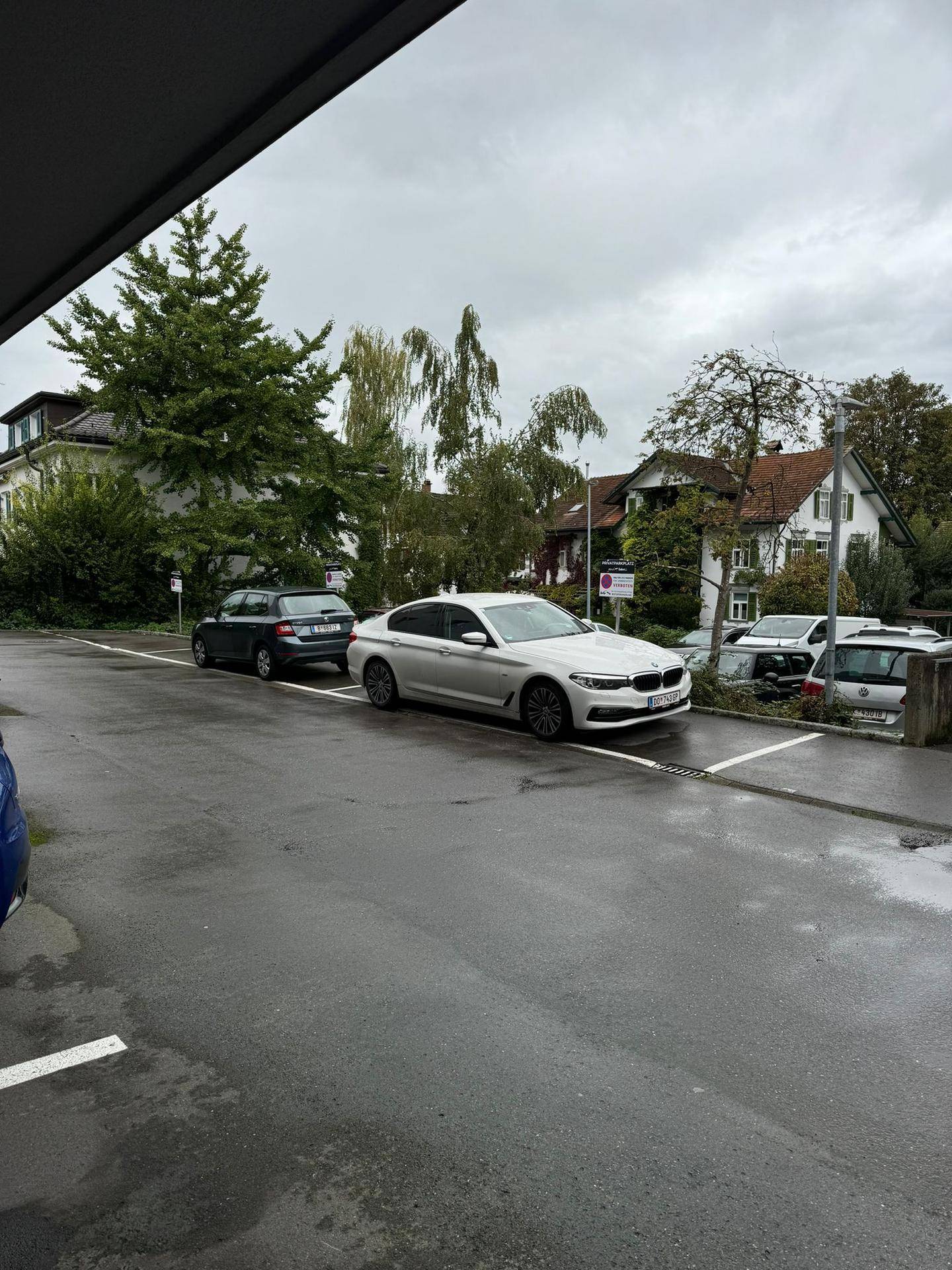 Straßenansicht mit geparkten Autos und Wohnhäusern unter bewölktem Himmel.