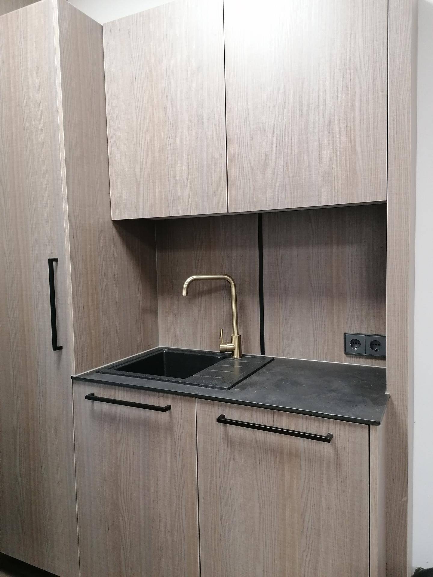 Moderne Küchenzeile mit Holzschränken, schwarzer Arbeitsplatte und goldfarbenem Wasserhahn.