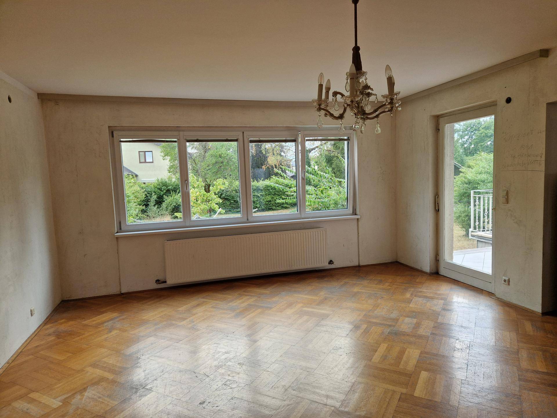 Helles Wohnzimmer mit Fischgrätparkett, großem Fenster und Zugang zur Terrasse.