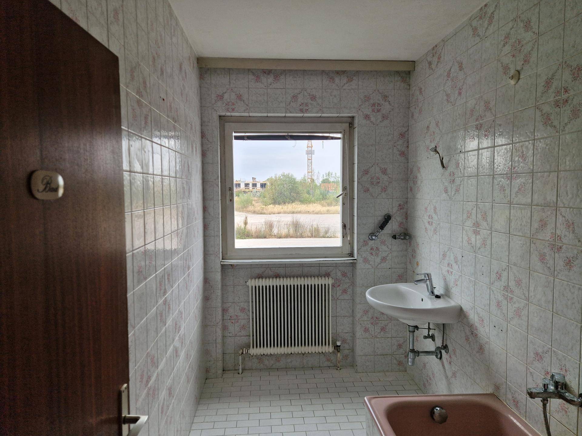 Badezimmer mit rosa Badewanne, Fenster und gemusterten Wandfliesen.