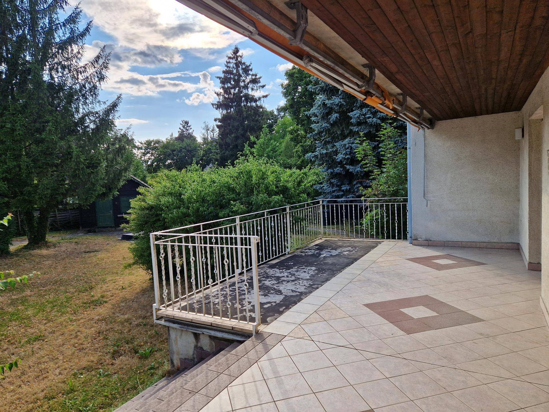 Geflieste Terrasse mit Geländer und Blick auf den weitläufigen Gartenbereich.