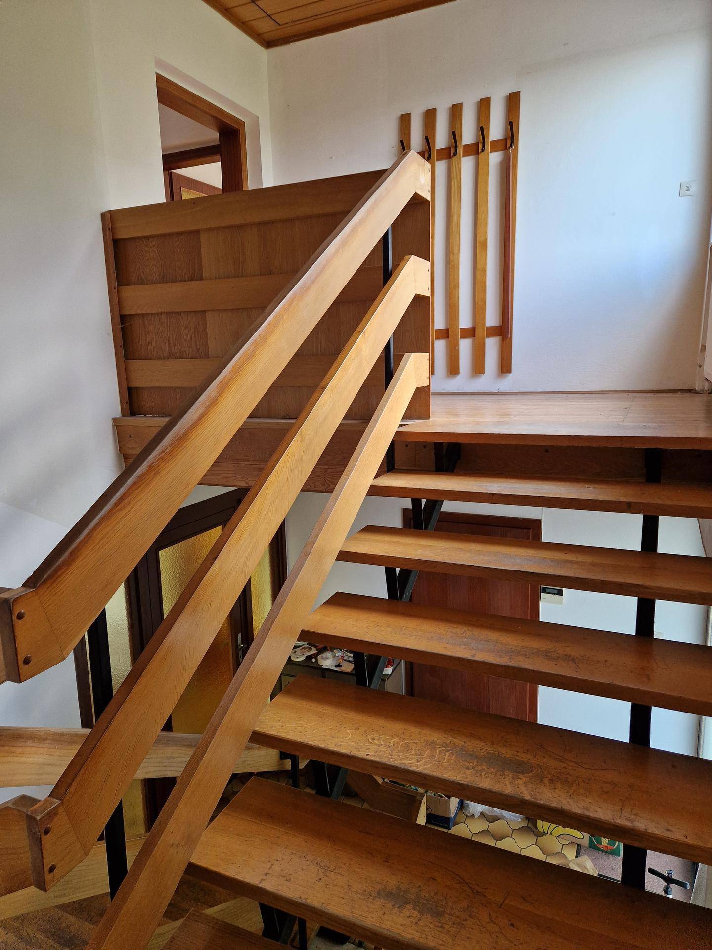 Holztreppe führt in das obere Stockwerk, mit Holzgeländer und Wandgarderobe.