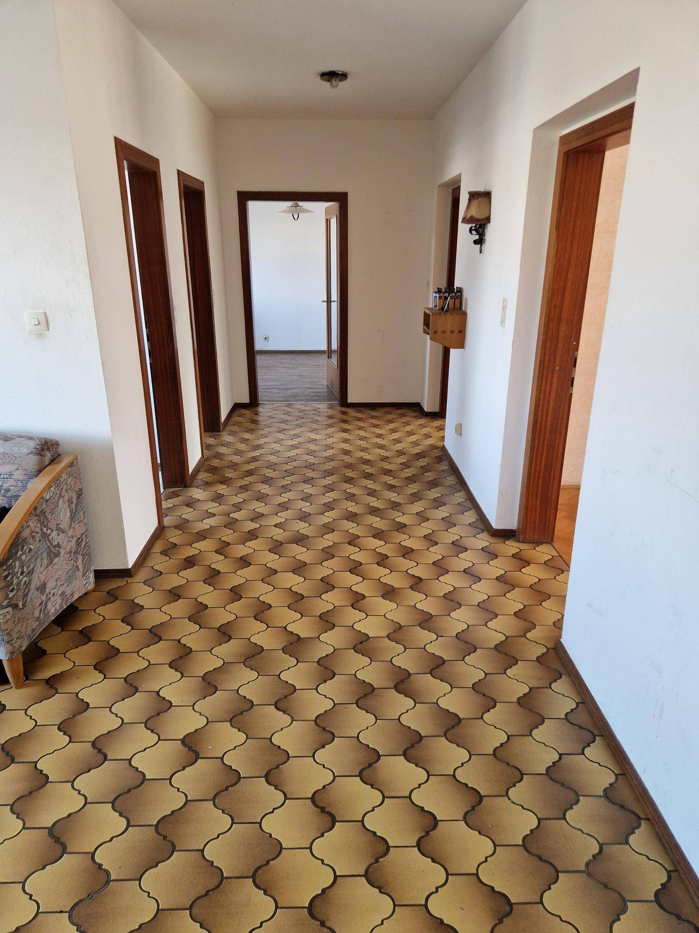 Langer Flur mit gemustertem Linoleumboden und Holztüren zu den angrenzenden Räumen.