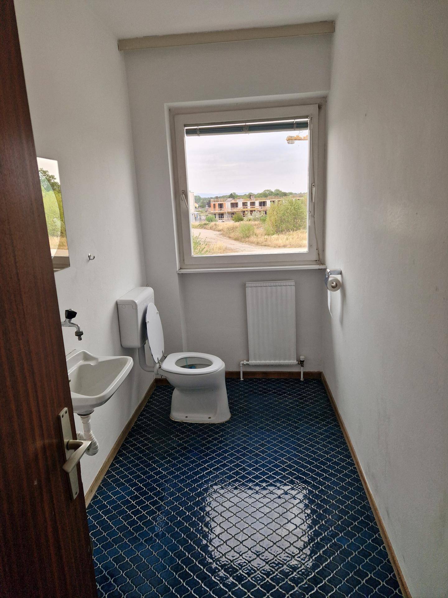 Kleines WC mit blauen Fliesen, Fenster und einfacher Sanitärausstattung.