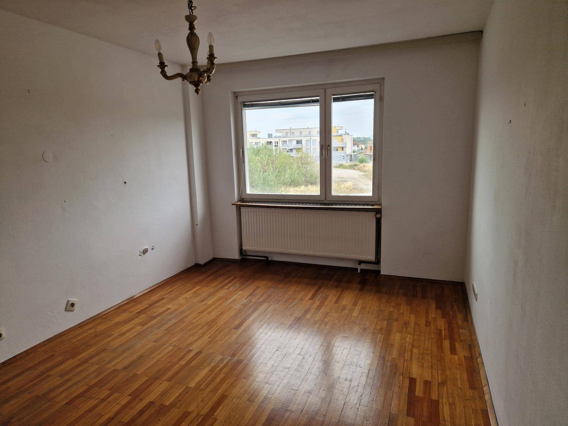 Schlafzimmer mit Parkettboden, großem Fenster und Blick auf die Umgebung.