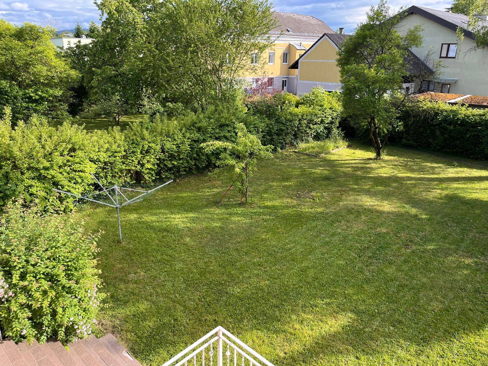 Großer, gepflegter Garten mit Rasenfläche und umliegenden Büschen und Bäumen.