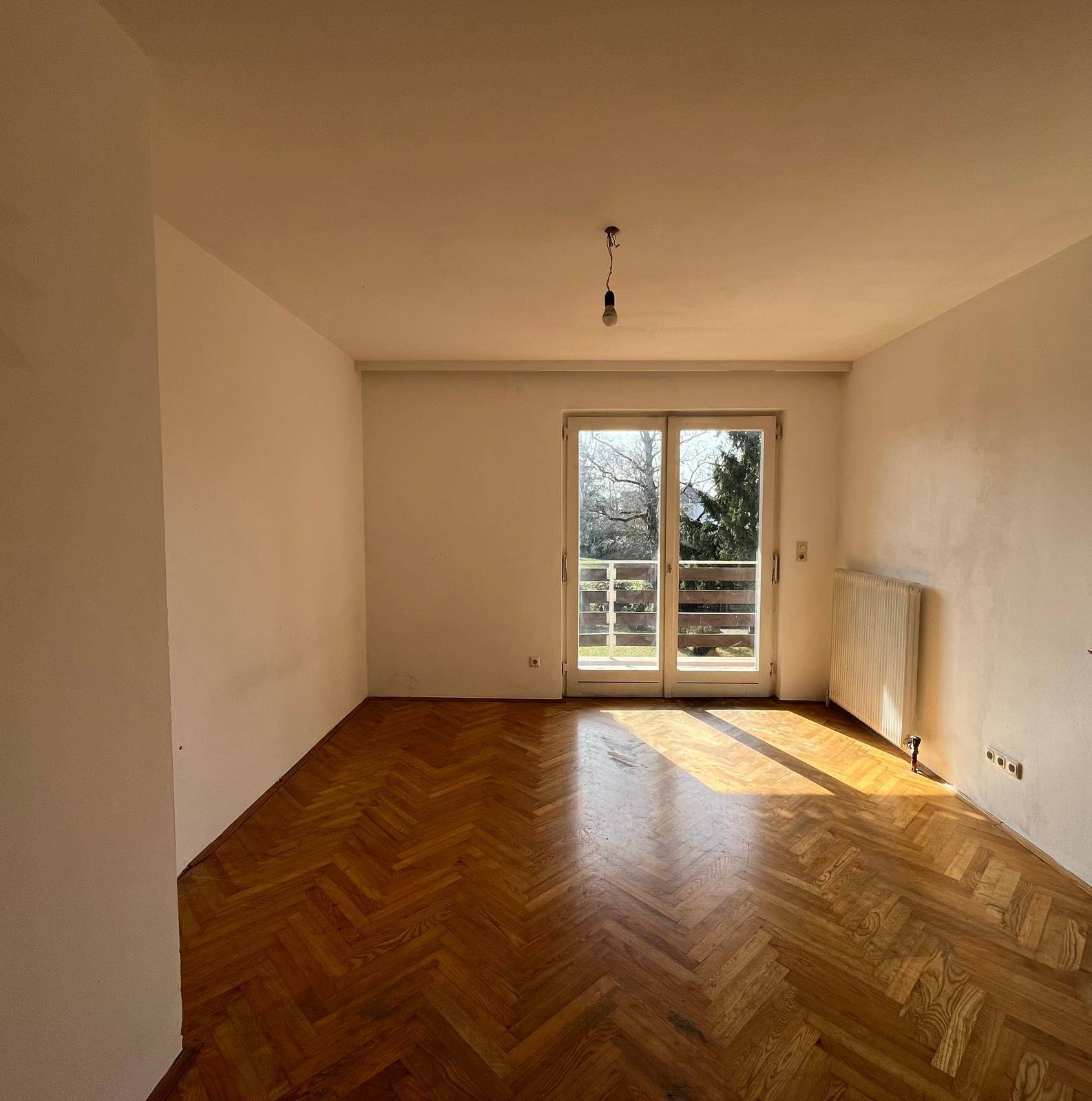Helles Schlafzimmer mit Fischgrätparkett und Balkontür, durchflutet von Sonnenlicht.