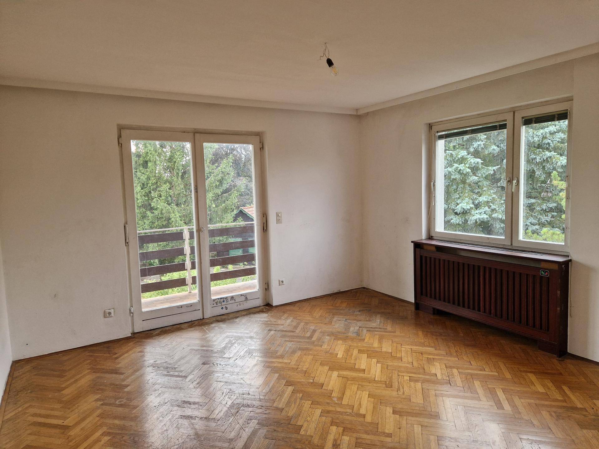 Schlafzimmer mit Parkettboden, Fenster und Balkontür mit Blick ins Grüne.