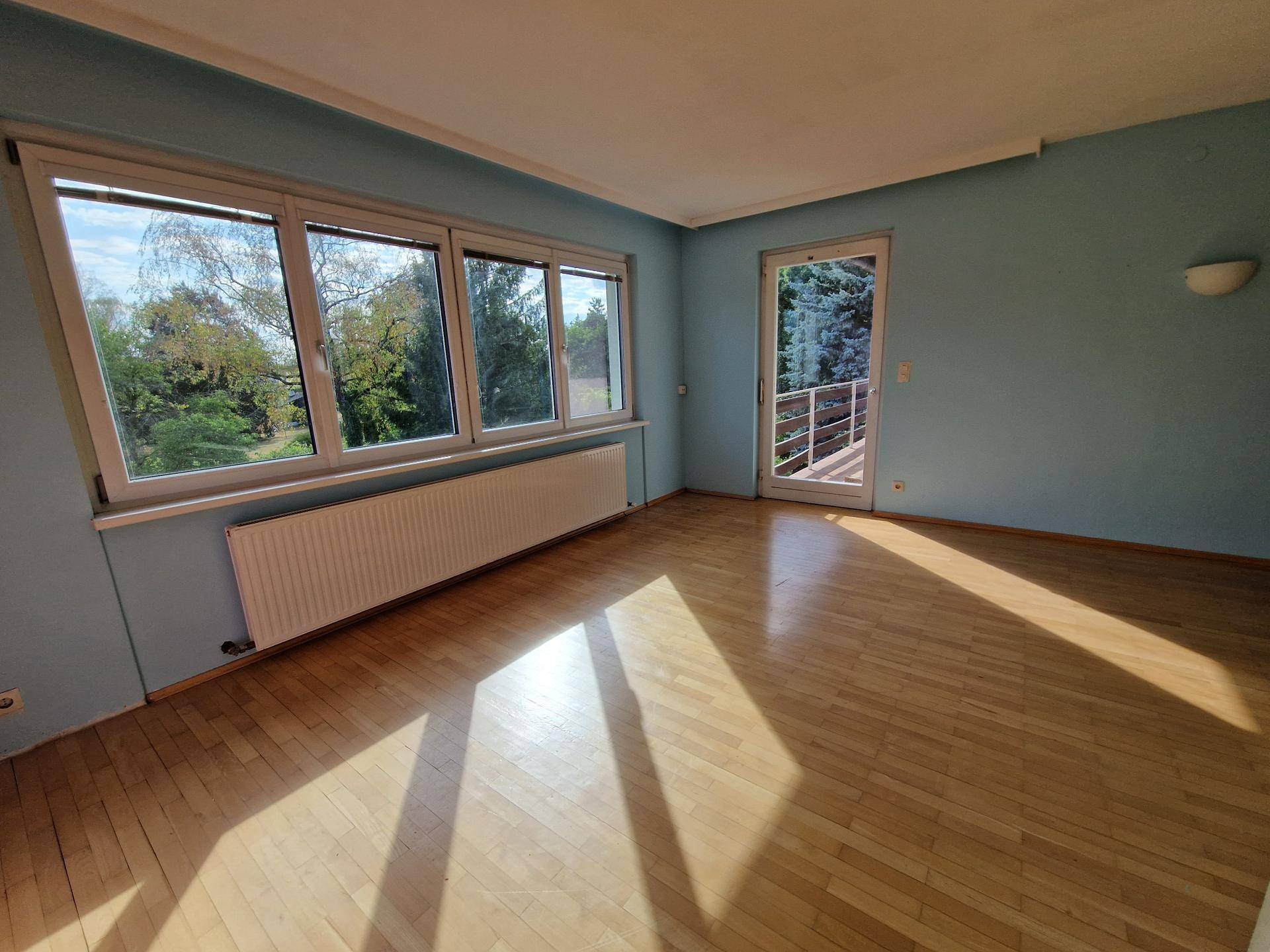 Schlafzimmer mit hellblau gestrichenen Wänden, Parkettboden und Zugang zum Balkon.