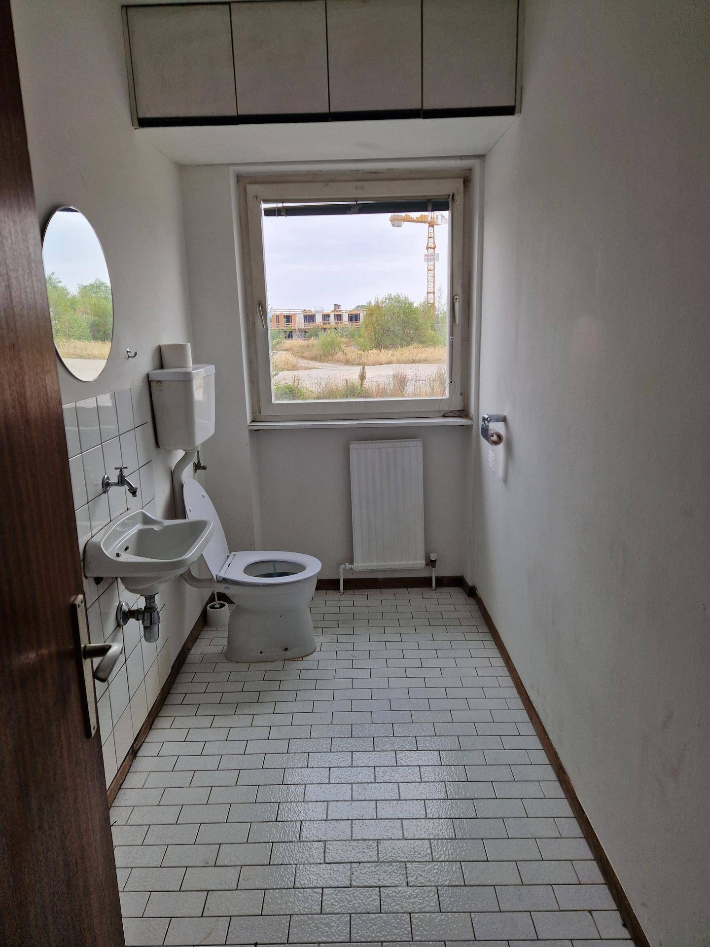 WC mit weißen Fliesen, Fenster und einfacher Sanitärausstattung.
