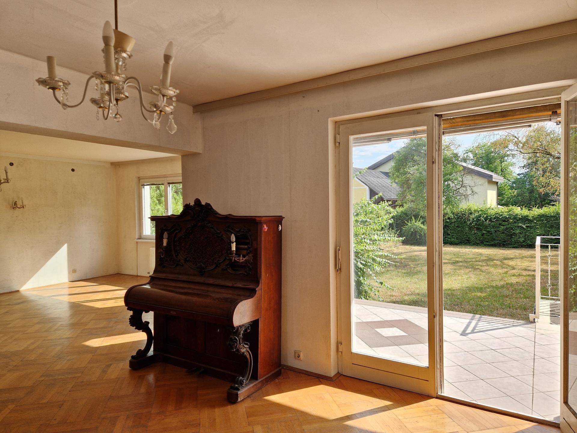 Geräumiges Wohnzimmer mit Parkettboden, Kronleuchter und direktem Zugang zur Terrasse.