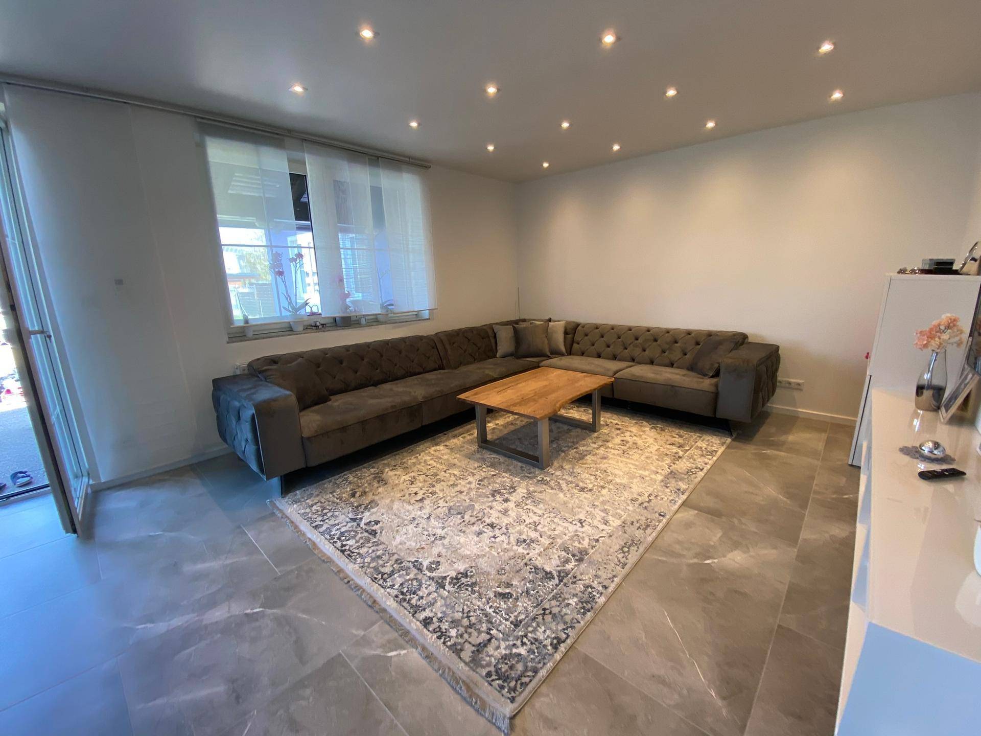 Gemütliches Wohnzimmer mit großem Ecksofa, Couchtisch und Teppich auf Fliesenboden.