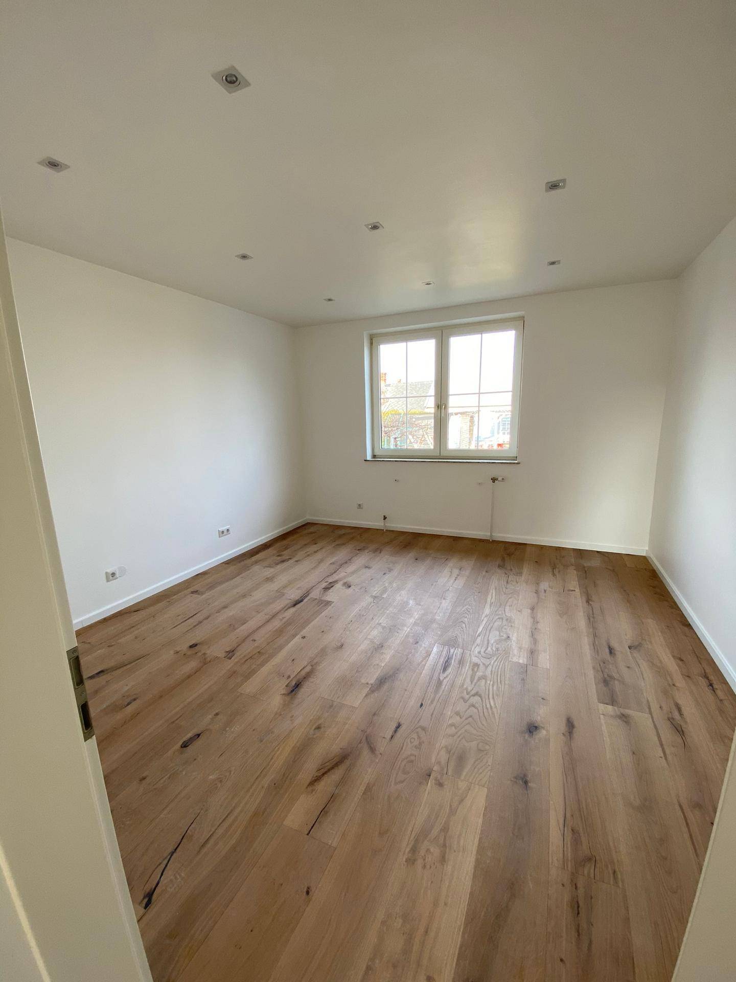 Helles Schlafzimmer mit neuem Holzboden, weißen Wänden und Einbaustrahlern an der Decke.