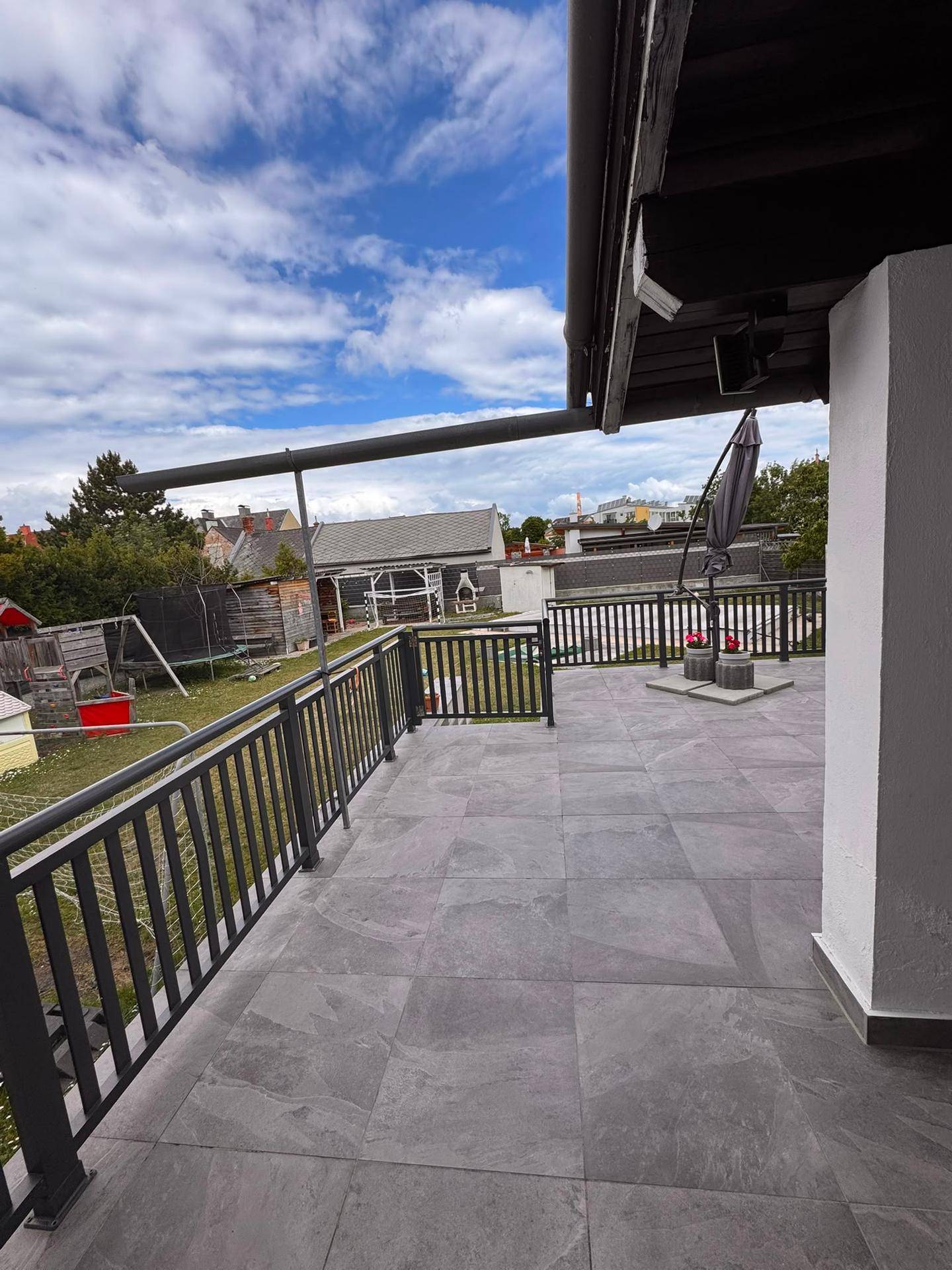 Große geflieste Terrasse mit modernem Geländer und Blick auf den Garten und die Umgebung.