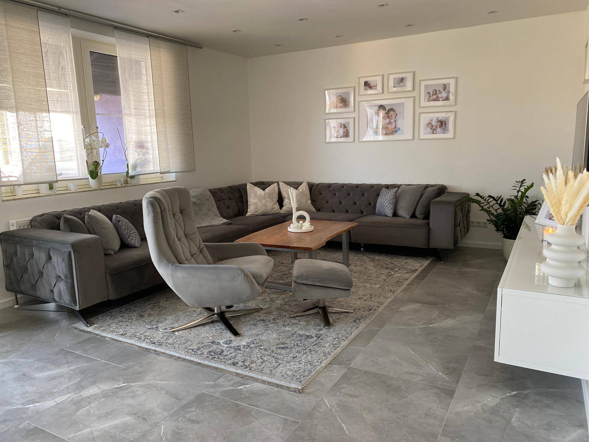 Modern eingerichtetes Wohnzimmer mit großem Ecksofa, Sessel und Teppich auf Fliesenboden.