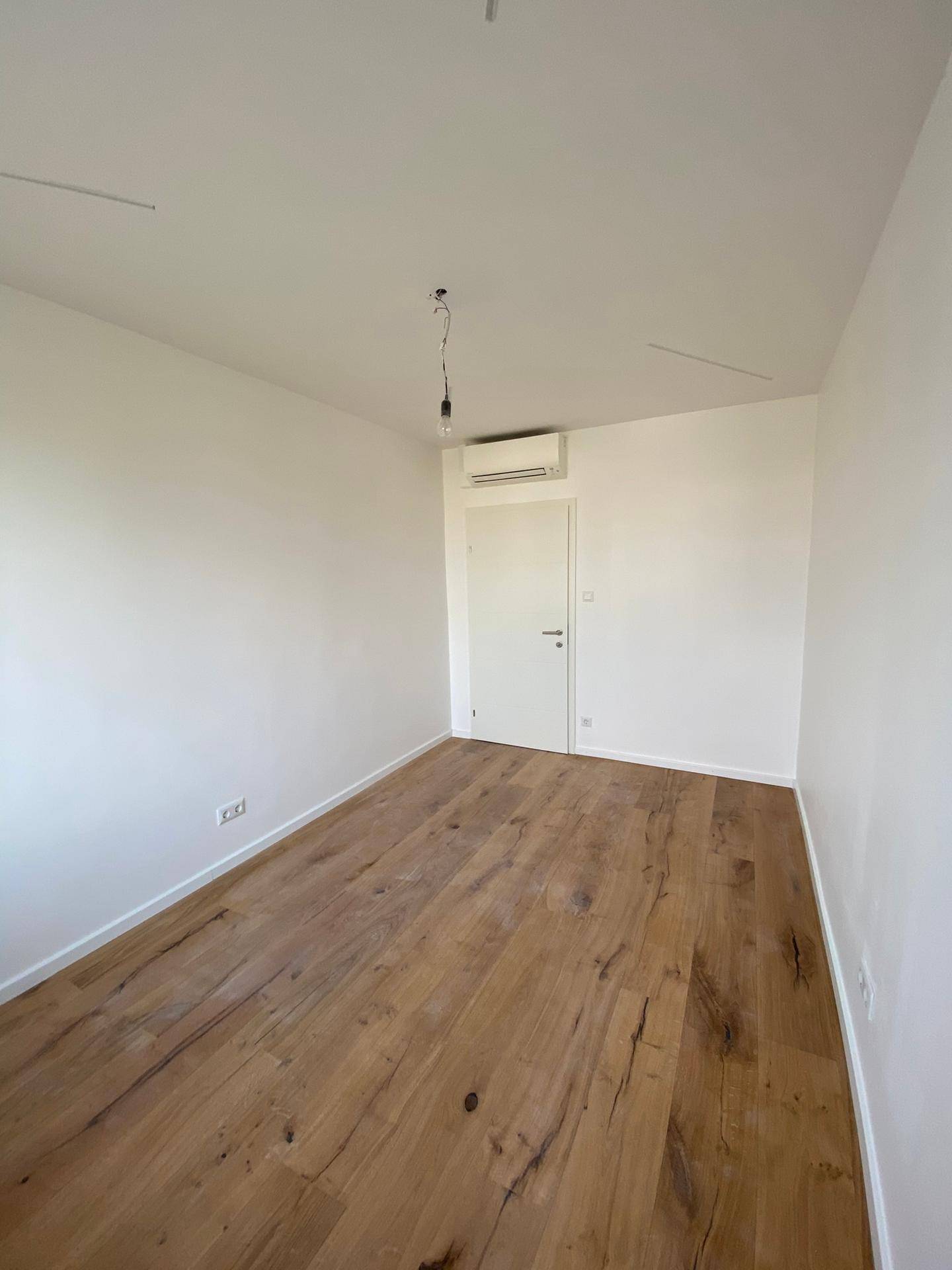 Schlafzimmer mit Holzboden, weißer Tür und Klimaanlage an der Wand.
