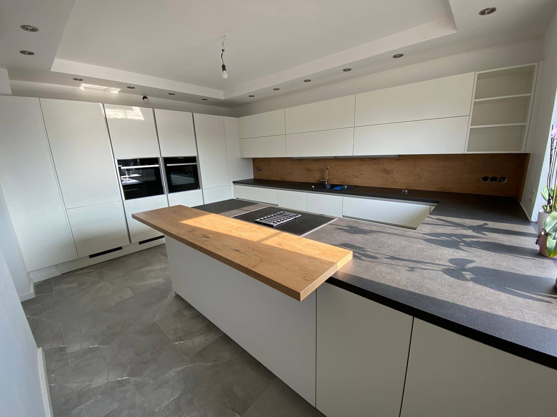 Moderne weiße Küche mit Kochinsel, integrierten Geräten und Holzdetails.