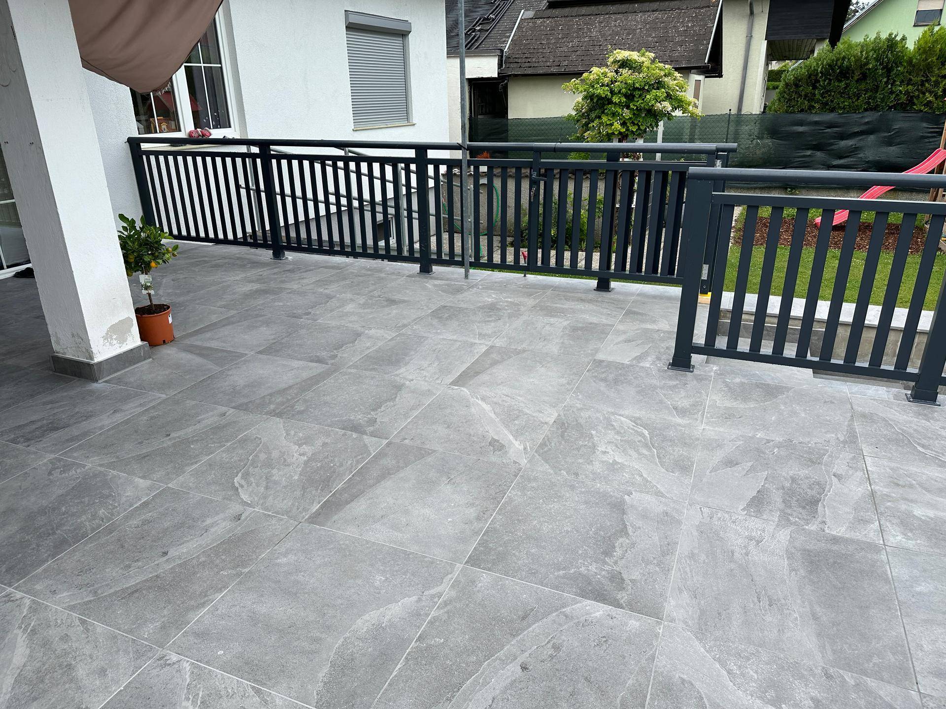 Geräumige geflieste Terrasse mit modernem Geländer und Blick auf den Gartenbereich.