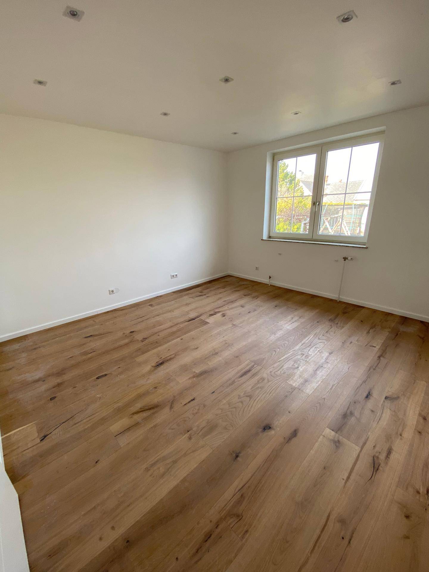 Geräumiges Schlafzimmer mit Holzdielenboden, weißen Wänden und großem Fenster.