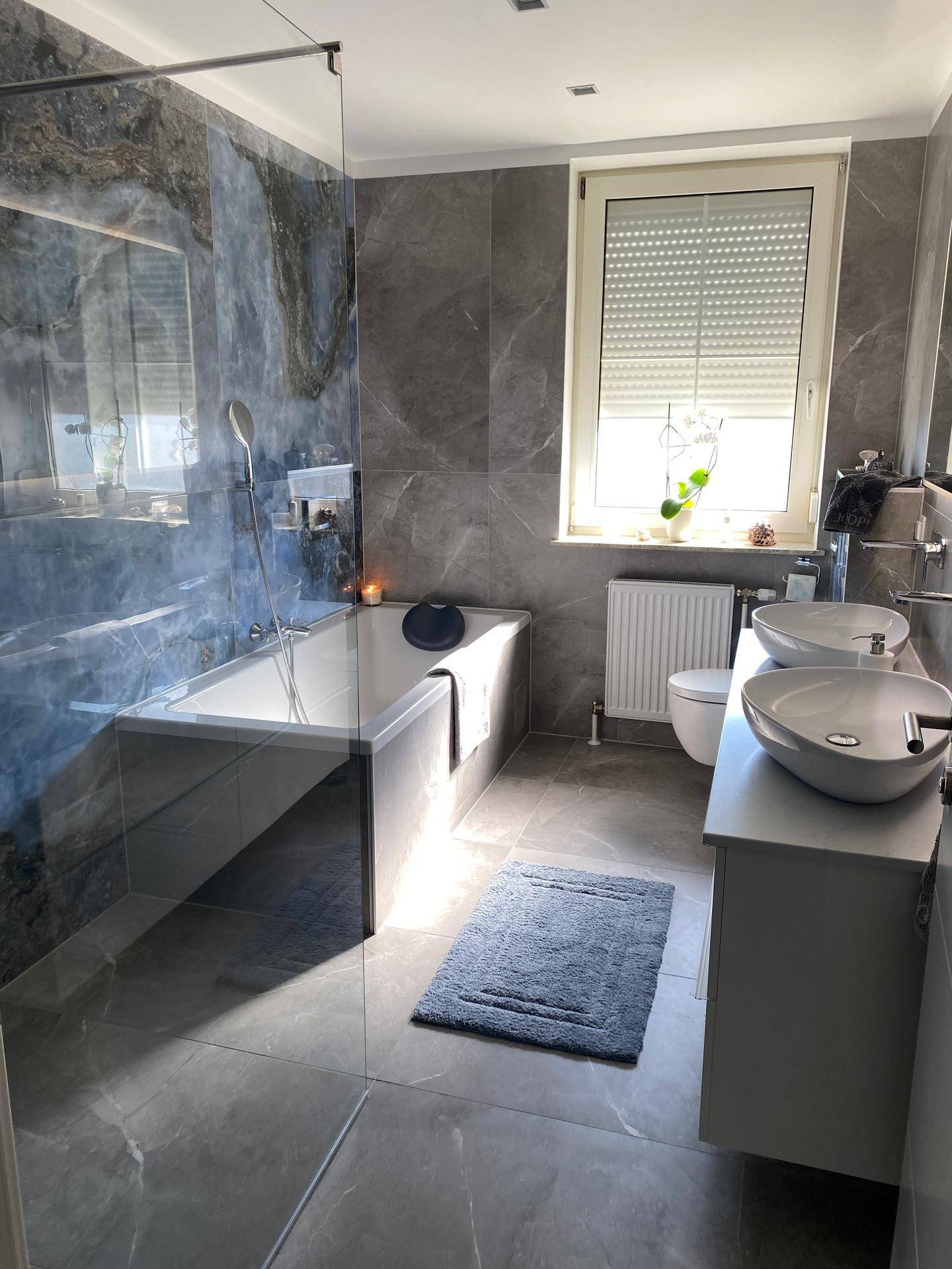 Helles Badezimmer mit Badewanne, Duschabtrennung, Doppelwaschbecken und Fenster.