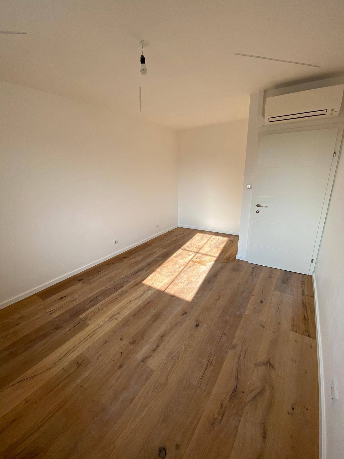 Schlafzimmer mit Holzboden, weißer Tür und Klimaanlage an der Wand.