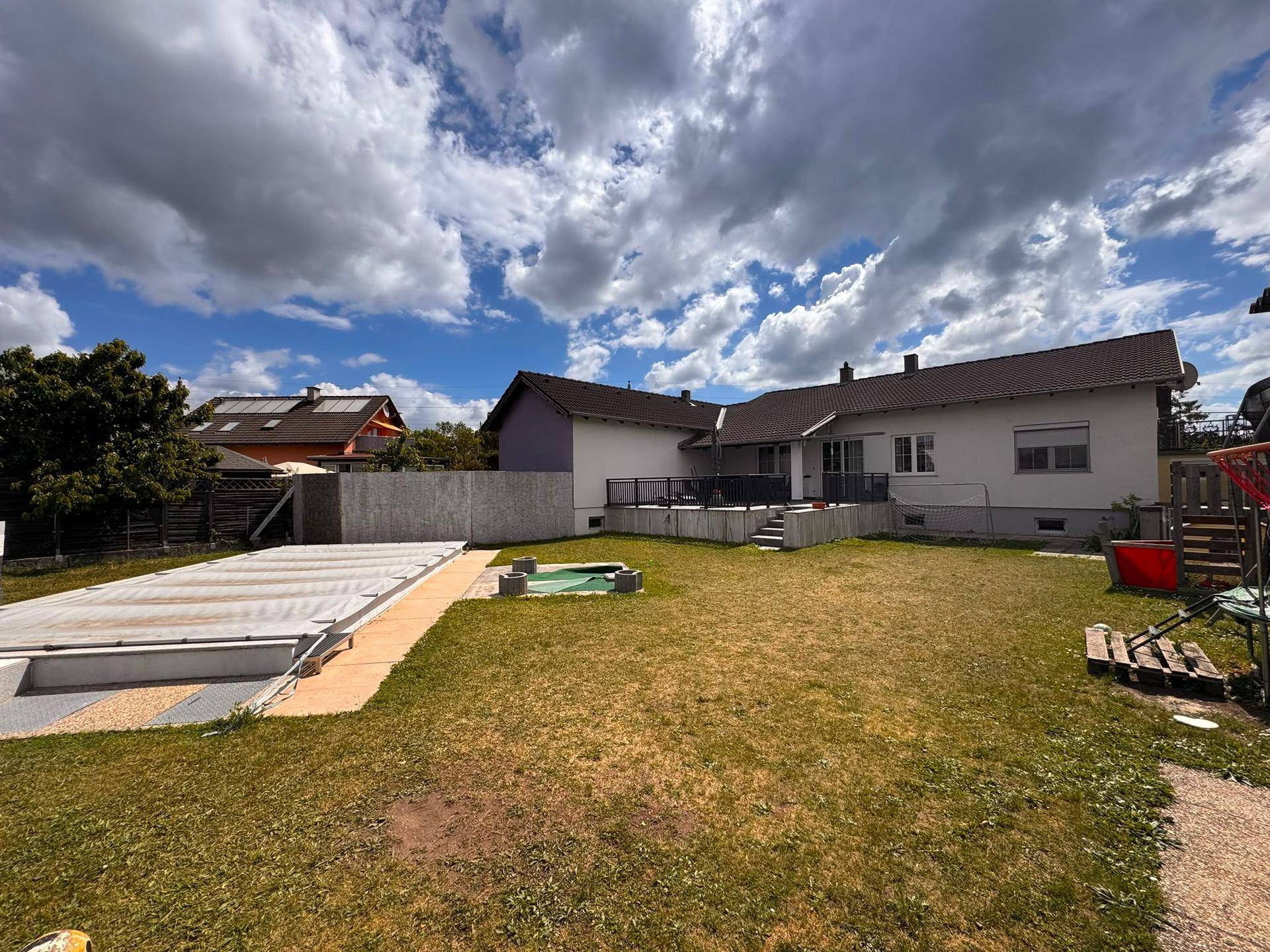 Großer Gartenbereich mit Rasenfläche, Poolabdeckung und Blick auf das Haus.