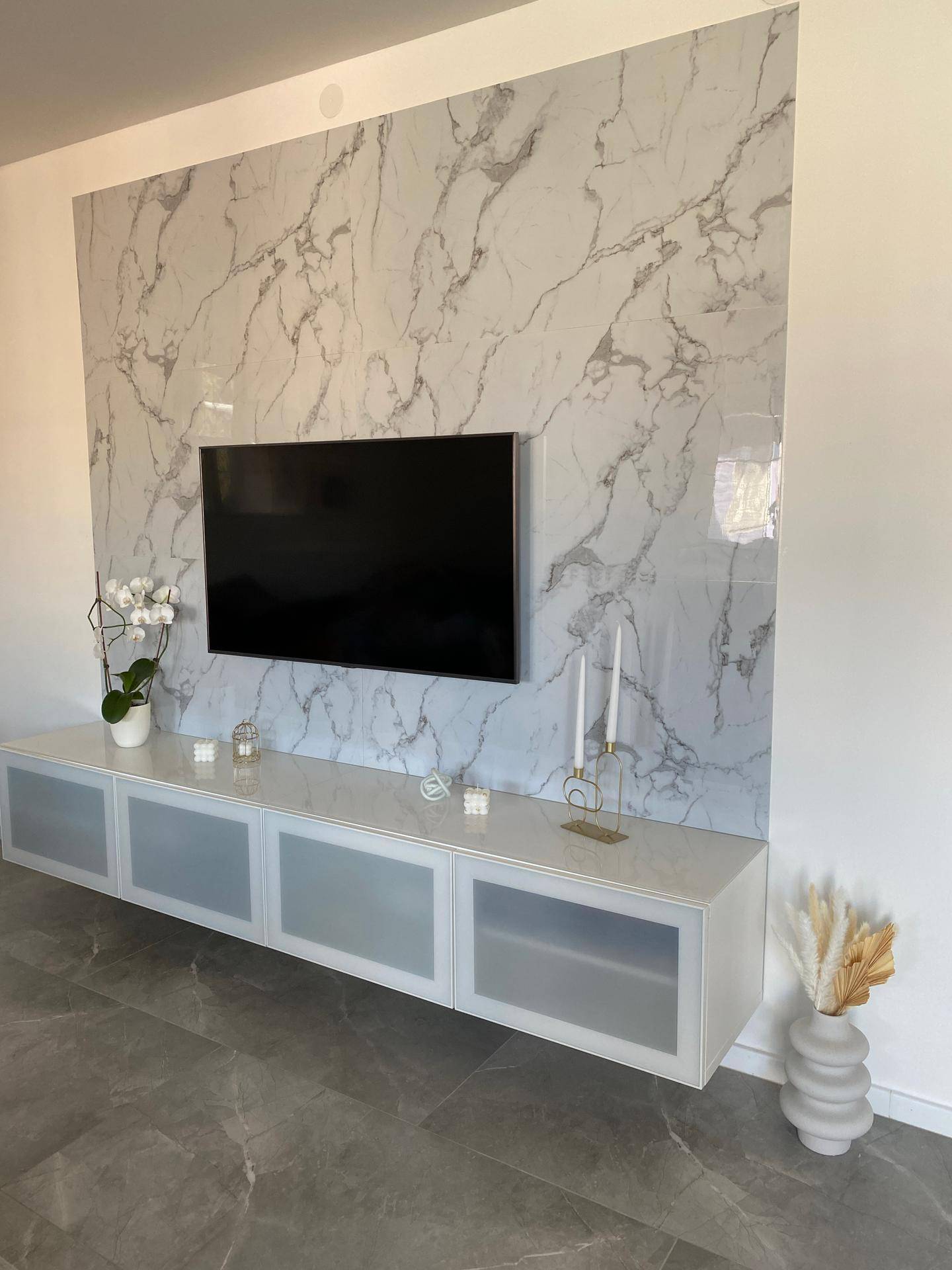 Wohnzimmer mit großem Fernseher an einer Marmorwand und schwebendem TV-Möbel.